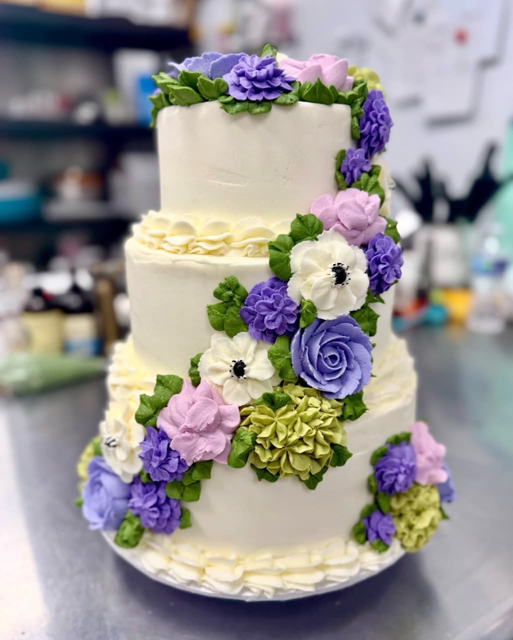 Three-tier custom wedding cake decorated with hand-piped purple, pink, and green flowers
