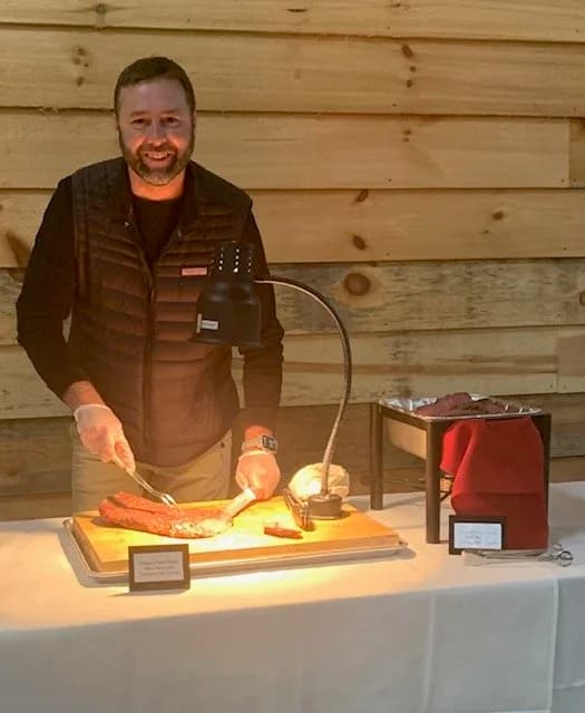 A carver slicing meat at a buffet station beneath a warming lamp.