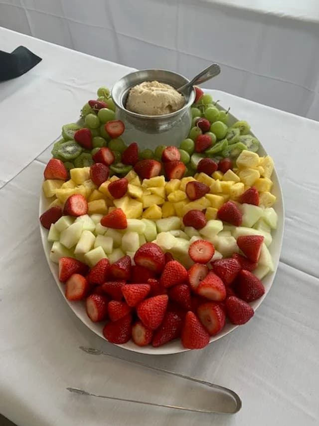 A platter of strawberries, melon, pineapple, and grapes with a bowl of cream.