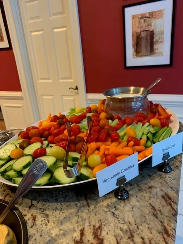 A divided vegetable crudité tray with tomatoes, cucumbers, carrots, and ranch dip.
