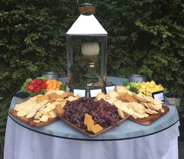 A cheese and fruit platter with grapes, crackers, and vegetables at an outdoor table.