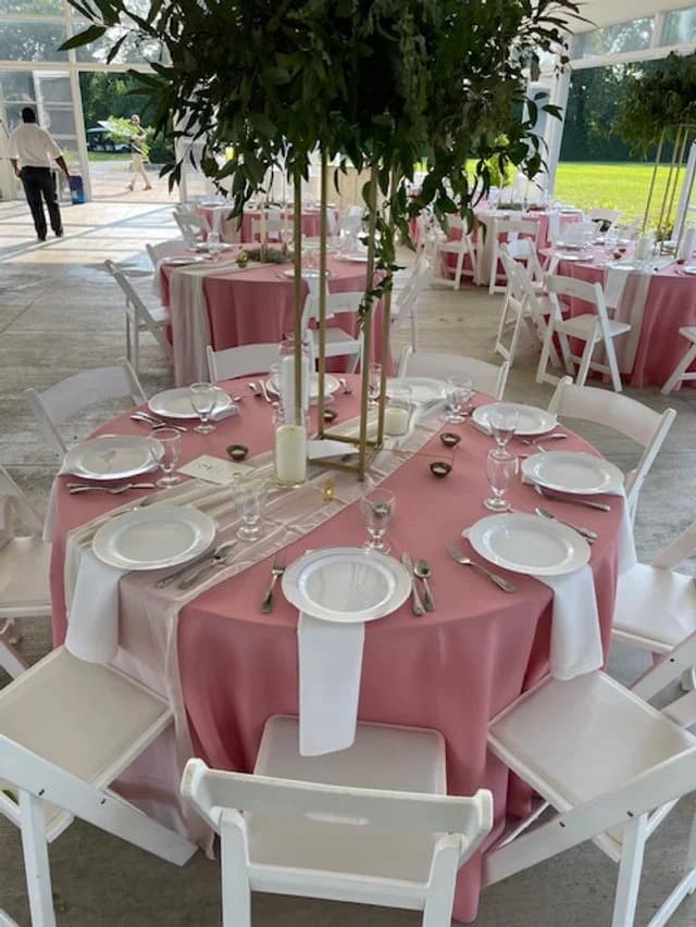 An elegant round table set with pink and white linens, glassware, and a floral centerpiece.