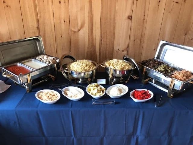 A buffet with pasta, chafing dishes, vegetables, salad, and toppings.