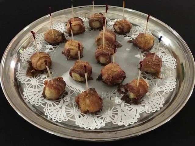 Bacon-wrapped appetizers arranged with toothpicks on a silver tray.