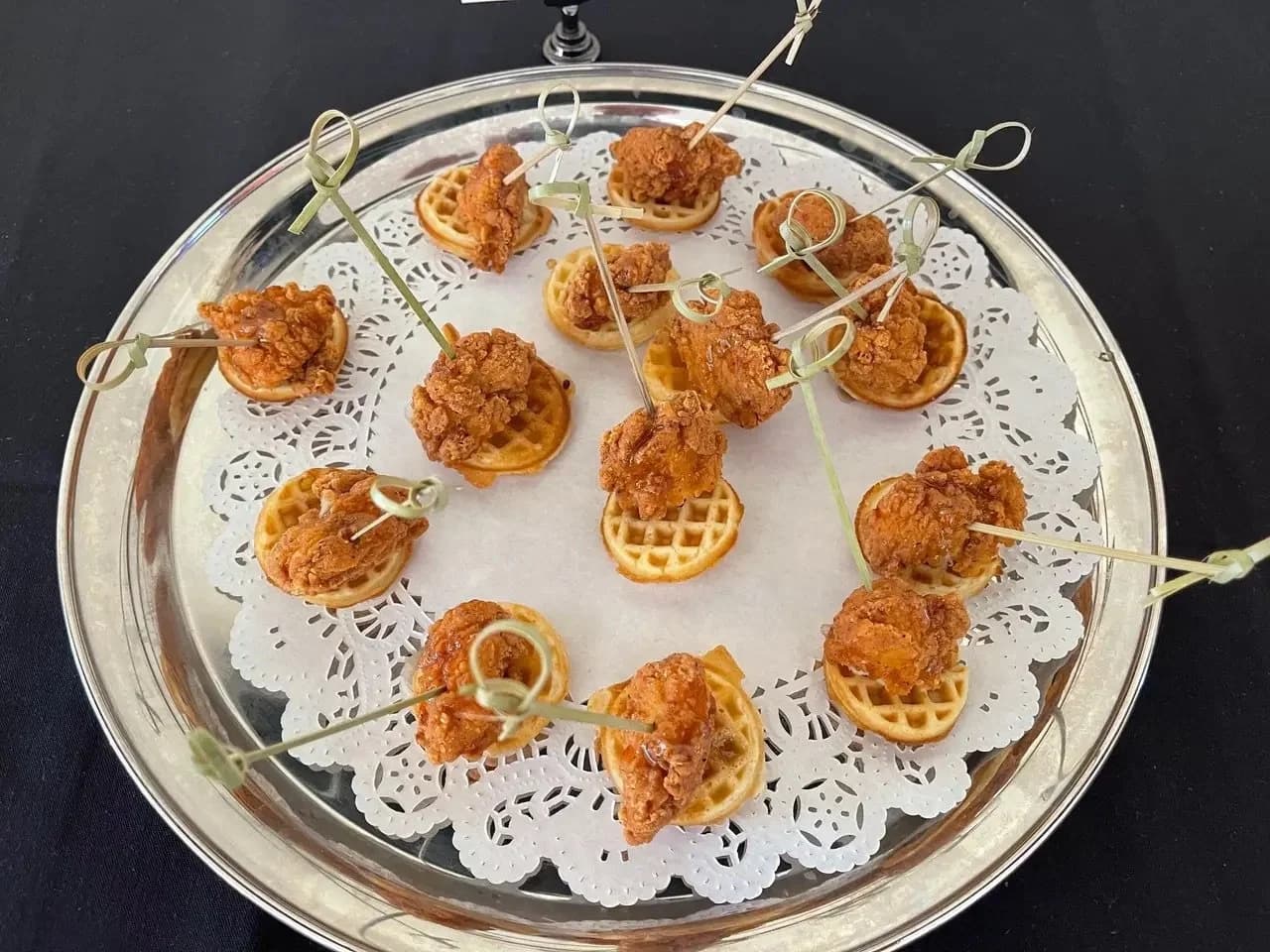 Mini chicken-and-waffle appetizers arranged on a silver serving tray.