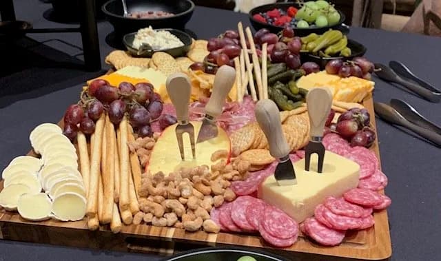 A charcuterie board with grapes, cheeses, crackers, cured meats, nuts, and cheese knives.