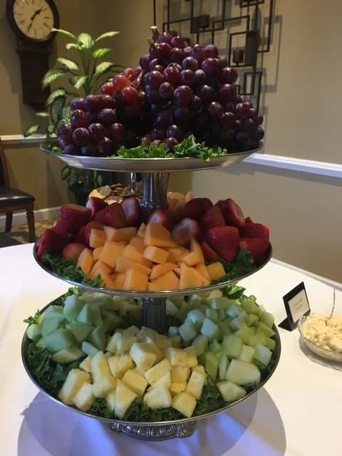 A three-tier serving stand filled with grapes, strawberries, cantaloupe, and honeydew.