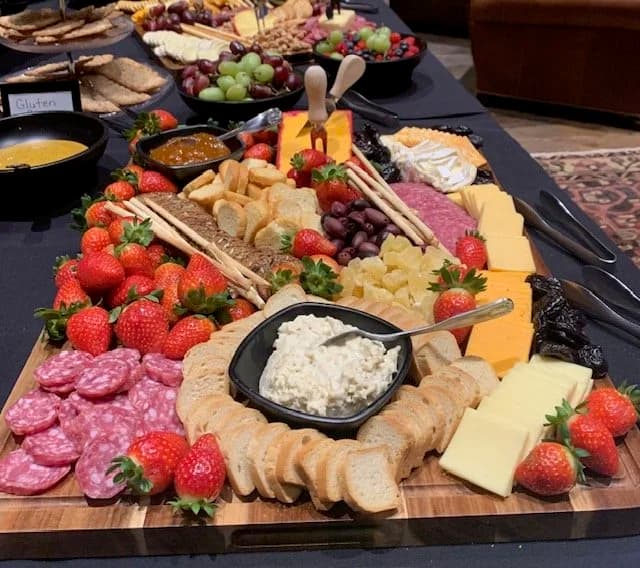 A wooden board filled with cheeses, cured meats, strawberries, grapes, crackers, and dipping sauces.