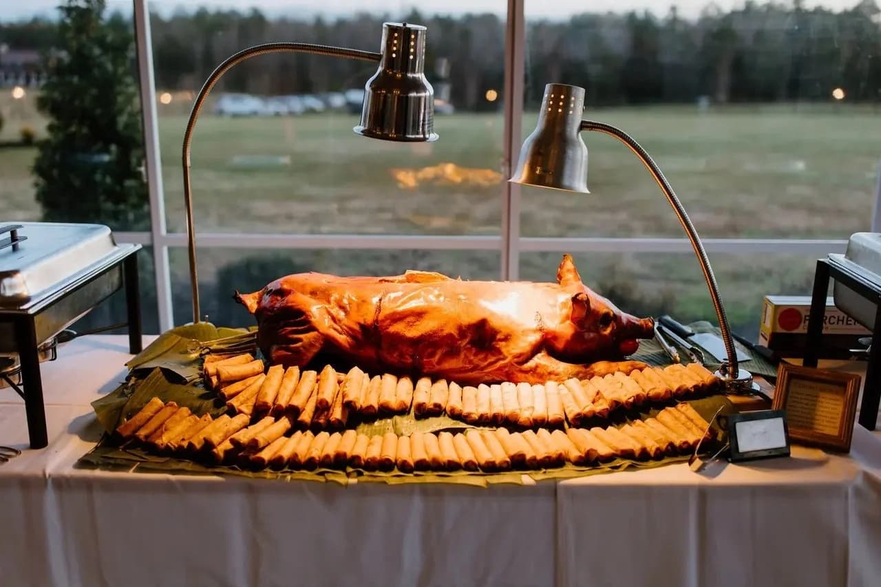 A whole-hog presentation surrounded by rolled appetizers beneath warming lamps.