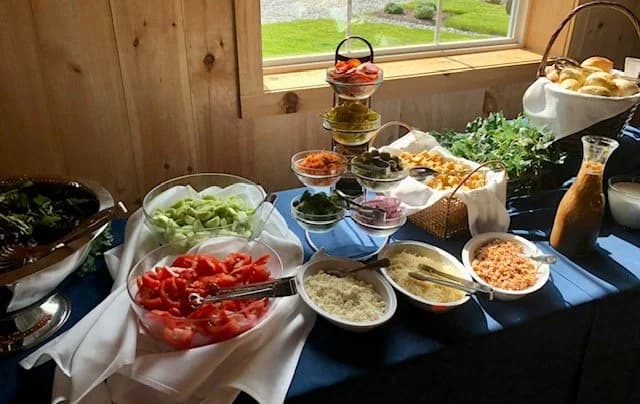 Fresh vegetables, salads, bread rolls, and condiments arranged on a buffet table.