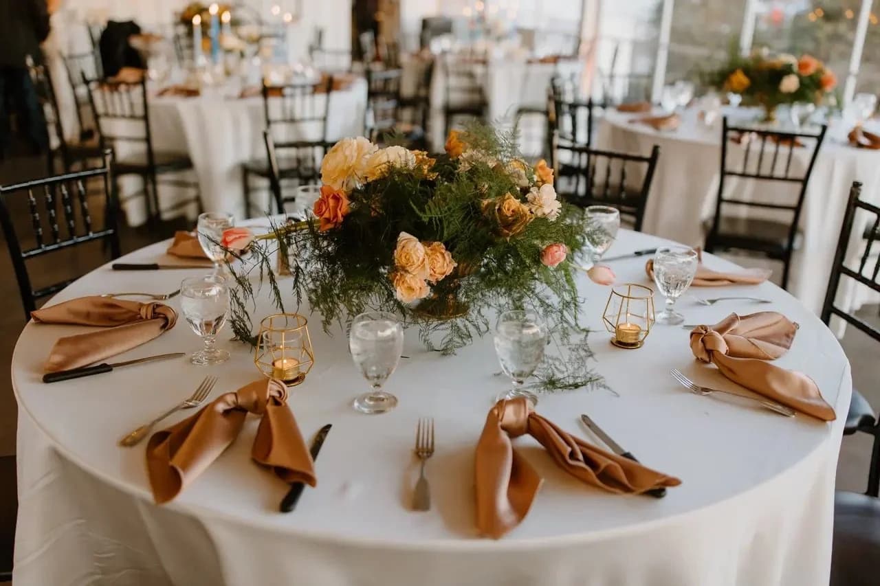 A formal banquet table with flowers, folded napkins, glassware, and gold candle holders.