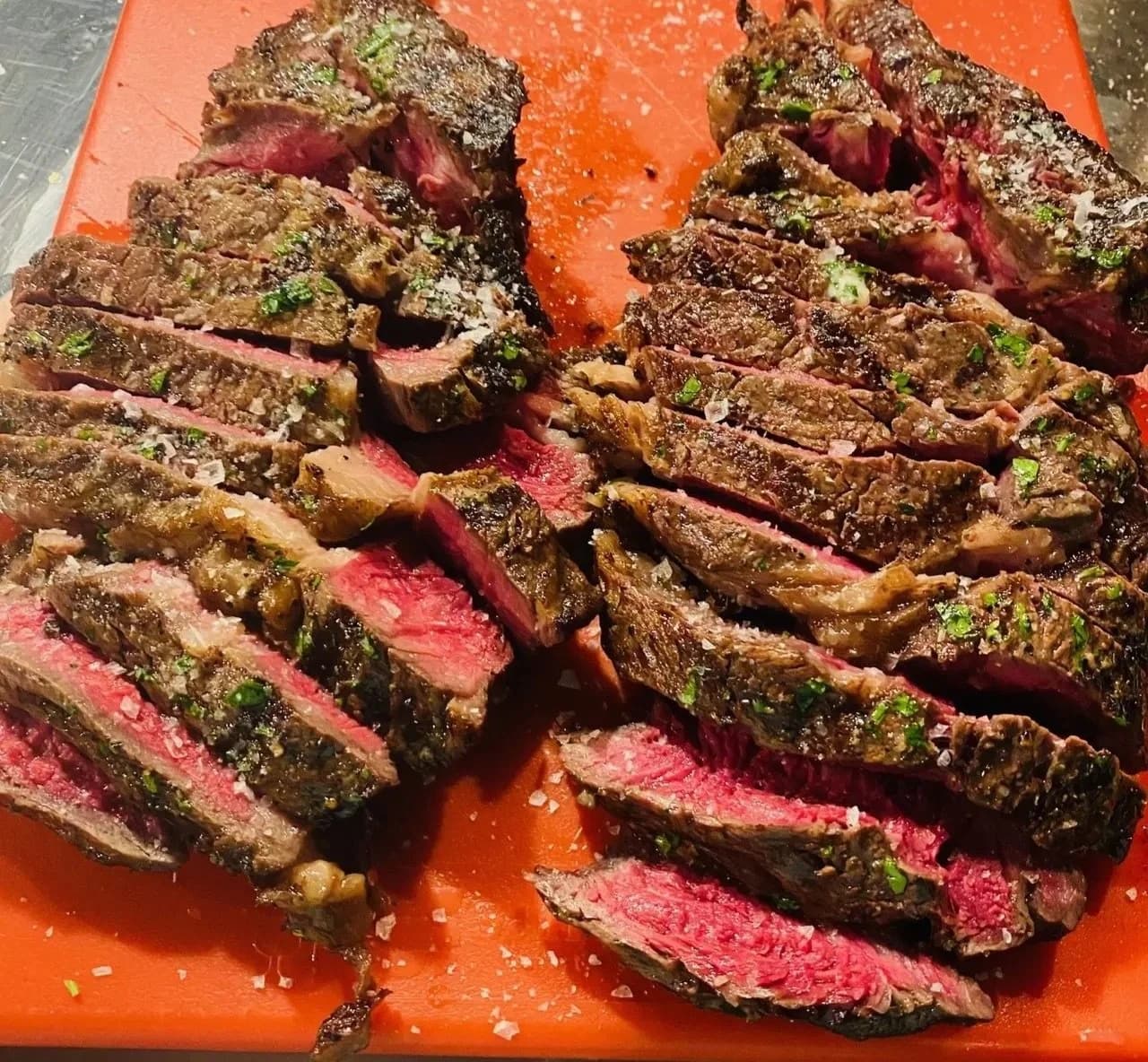 Slices of cooked steak with a pink center, herbs, and salt on a cutting board.