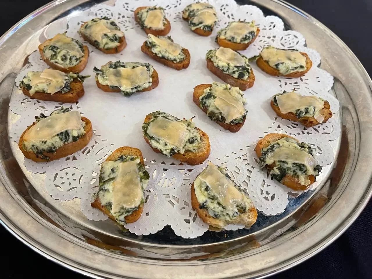 Toasted crostini topped with spinach and melted cheese on a silver tray.