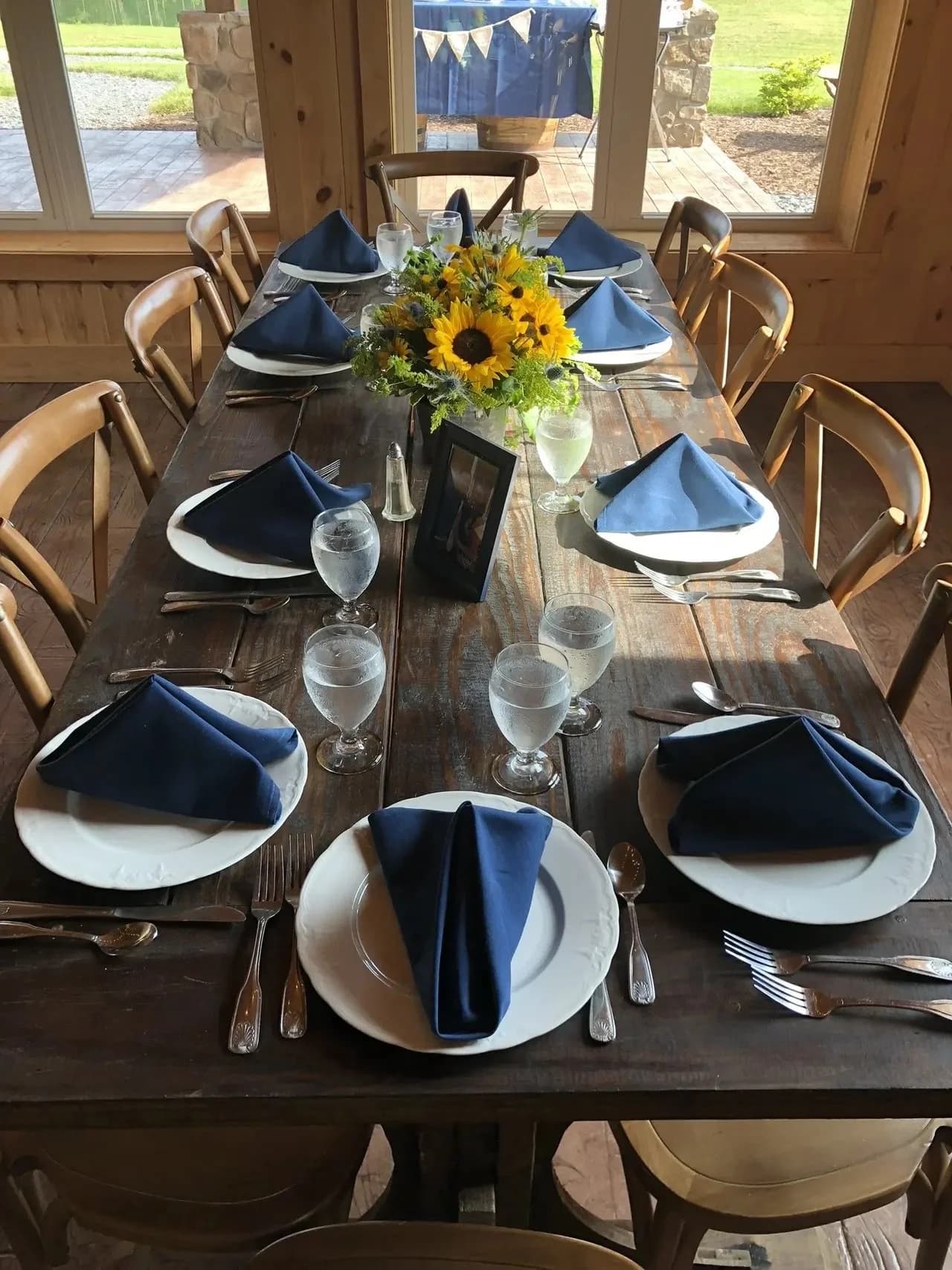 A dining table set with white plates, navy napkins, water glasses, and sunflowers.