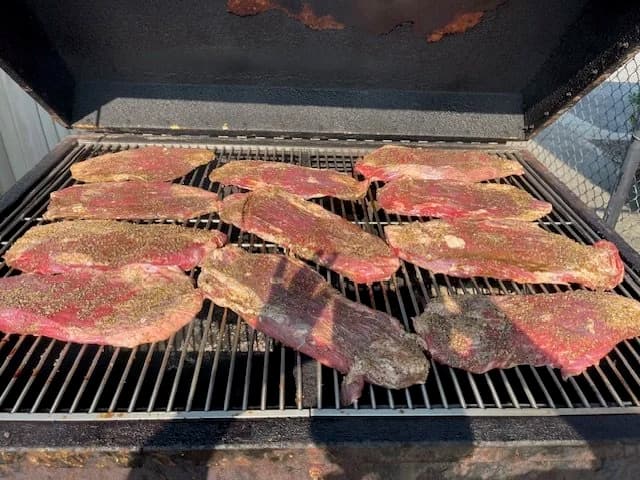Seasoned beef brisket slow-cooking on a grill.
