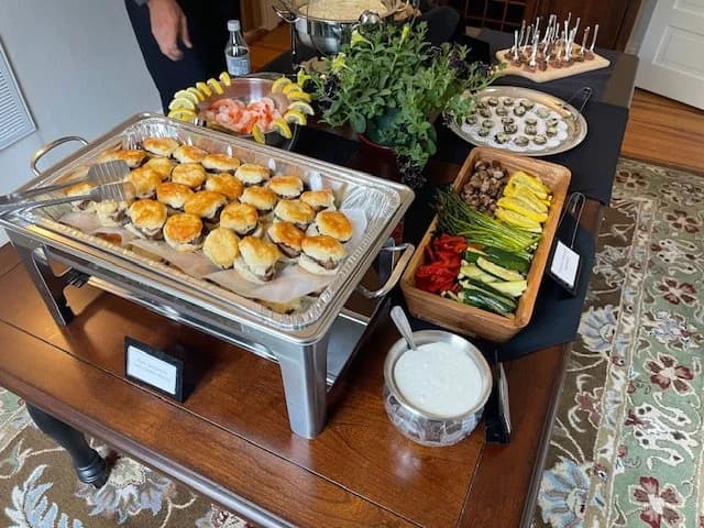 A table filled with sliders, seafood, stuffed mushrooms, vegetables, and dips.